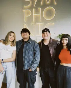 Four team members stand together in front of a wall with "SYMPHONIC" in neon lights, posing for a group photo.